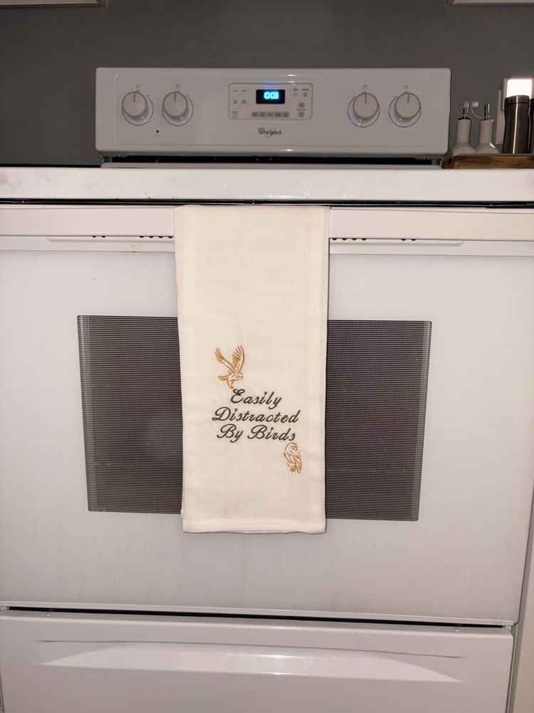 Linen kitchen towel with satin-stitch script and fine-line bird accents