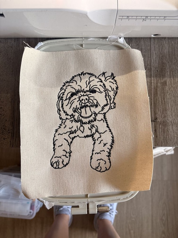 Canvas patch with a fine-line pet portrait, captured mid-stitch on the machine